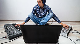 young man with  laptop and two synthesizers sitting on the floor. the process of creating electronic music