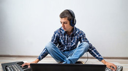 young man with  laptop and two synthesizers sitting on the floor. the process of creating electronic music
