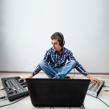 young man with  laptop and two synthesizers sitting on the floor. the process of creating electronic music